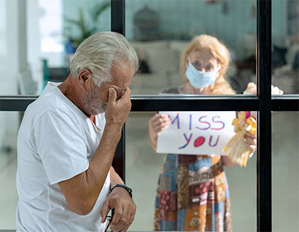 A man is behind a window crying whilst his wife is outside holding a sign saying 'Miss you'.