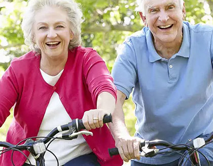 An elderly couple are sitting on bicycles and smiling.