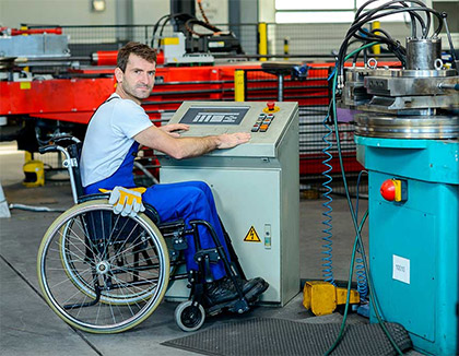 A man in a wheel chair is wearing protective clothing and is operating an industrial machine.