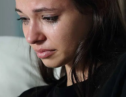 A young women is holding a mobile phone whilst crying.